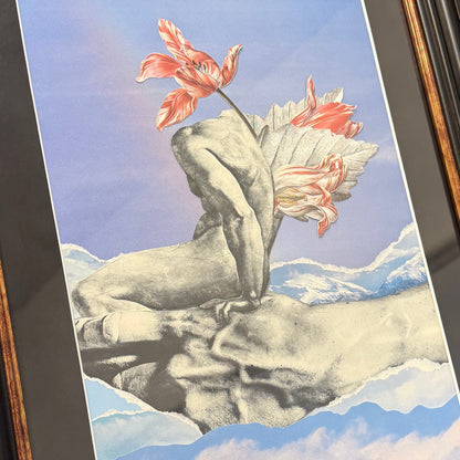 A framed surreal art print depicting a grayscale classical statue hand supporting a human torso, with red and white tulip flowers blooming from the back, set against a blue sky and mountain landscape.